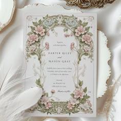 an ornate wedding card with flowers and feathers on the table next to other items such as brooches