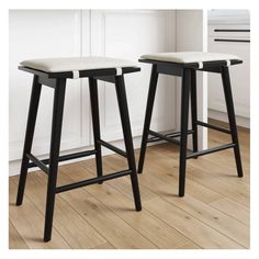 two black and white stools sitting on top of a wooden floor next to each other