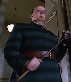 a man dressed in an old fashioned uniform holding a cane and looking off into the distance