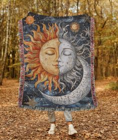 a woman standing in the woods holding up a blanket with a sun and moon on it