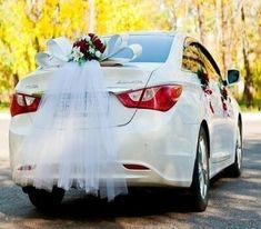 a white car with a bow tied to it's tail sitting on the road