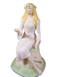 a figurine of a woman sitting on top of a green hill with flowers in her hair