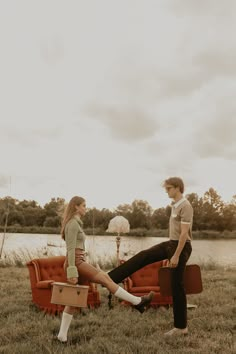 a man standing next to a woman sitting on top of an orange couch in a field