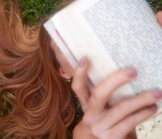 a woman laying on the ground reading a book with her eyes closed and hair blowing in the wind