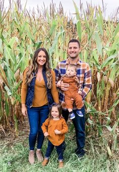 a man, woman and child standing in front of a cornfield with the baby holding him