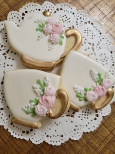 three decorated cookies sitting on top of a doily with lace and flowers in the shape of teapots