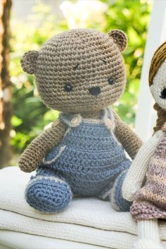 two crocheted teddy bears sitting next to each other on top of a pillow