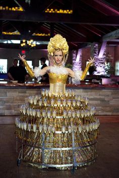 a woman dressed in gold is standing next to a large stack of champagne glasses on display