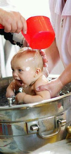 a baby is being bathed in a large metal bowl with water from a faucet