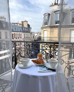 there is a table with two cups and a croissant on it in front of the window