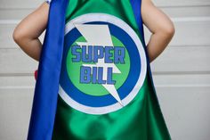 a little boy dressed in a green and blue cape with the word super bill printed on it