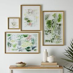 four framed pictures hang on the wall above a table with a vase and plant in it