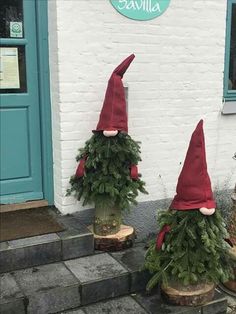 two gnomes made out of christmas trees sitting on the side of a building next to a fire hydrant