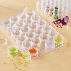 several plastic containers filled with different colored beads on top of a wooden table next to each other