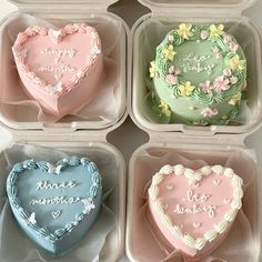 four heart shaped cakes in plastic containers with writing on the top, and flowers around them