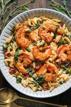 pasta with shrimp and spinach in a white bowl on top of a wooden table