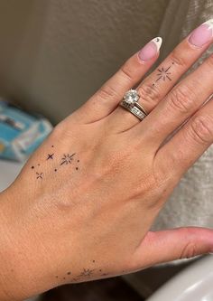 a woman's hand with two rings on it and stars tattooed on the ring finger