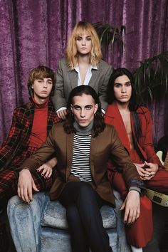 four people sitting on top of a chair in front of a purple curtain with curtains behind them