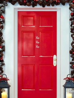 a red front door with christmas decorations around it and two lanterns on the ground next to it