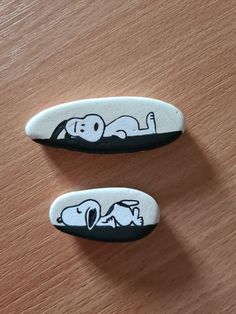 two black and white rocks with cartoon characters on them sitting on a wooden table next to each other