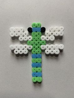 a cross made out of buttons and plastic beads on a white surface with clouds in the background