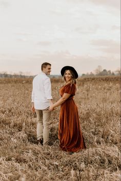 a man and woman are standing in the middle of a field holding hands while looking into each other's eyes