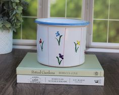 two books are stacked on top of each other next to a flower pot with flowers painted on it