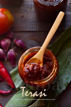 a jar filled with chili sauce next to some red peppers and green leaves on a wooden table