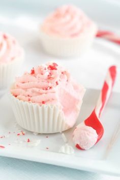 three cupcakes with pink frosting and candy cane on a white square plate