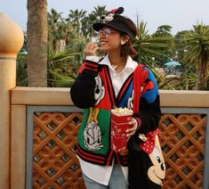 a woman in mickey mouse ears eating popcorn and talking on her cell phone while standing next to a fence