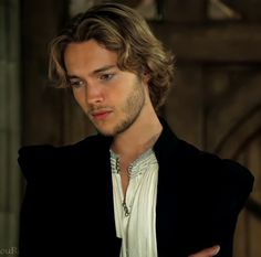 a man with long hair wearing a black jacket and white shirt looking at the camera