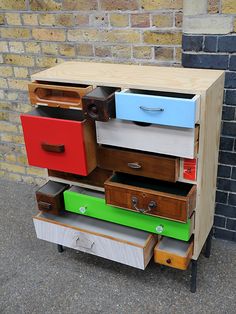 multicolored drawers are stacked on top of each other in front of a brick wall