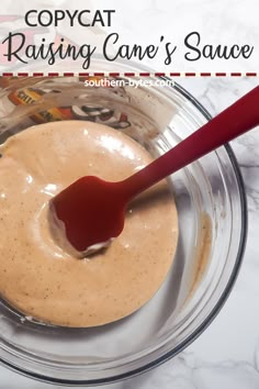 a glass bowl filled with sauce on top of a marble counter next to a red spoon