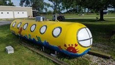 a large yellow submarine shaped tank sitting on top of a lush green field next to a building