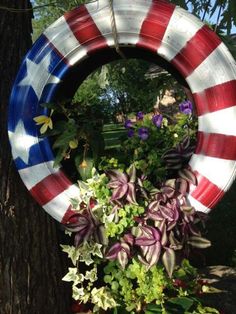 an american flag wreath hanging on a tree in front of some flowers and plants,