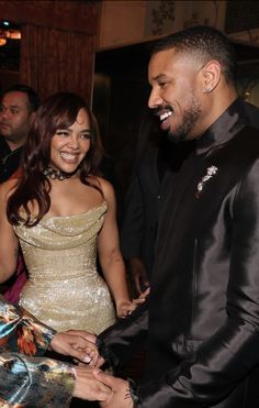 a man and woman standing next to each other at a formal event, shaking hands