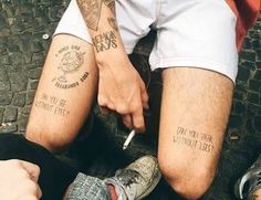 two people sitting on the ground with their legs crossed and one person has tattoos on his leg