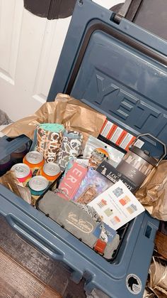 an open blue cooler filled with lots of food and drink items on top of a wooden floor