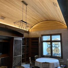 a dining room with a round table surrounded by chairs and wine racks in the background