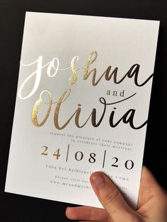 a hand holding up a white and gold wedding card