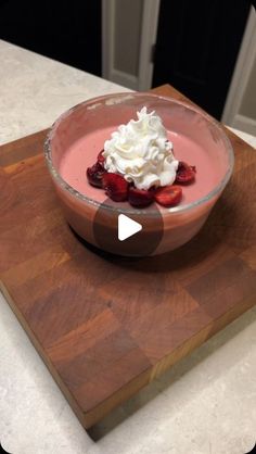 a bowl filled with whipped cream and strawberries on top of a wooden cutting board