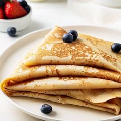 stack of pancakes with blueberries and syrup on white plate next to bowl of strawberries