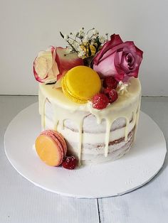 a white cake with flowers and macaroons on top, sitting on a plate