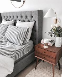 a bedroom with a bed, nightstand and mirror on the wall next to an end table