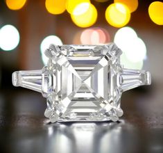 an emerald - cut diamond ring sits on a table in front of boke lights