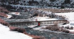 a train traveling across a bridge over a snow covered river in the middle of winter