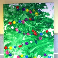 an art project is displayed on the wall in front of a green christmas tree with multicolored ornaments