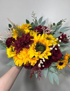 a bouquet of sunflowers and other flowers is being held by a person's hand