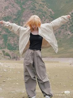 a woman standing on top of a grass covered field with her arms spread wide open