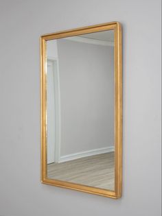 a gold framed mirror on the wall in an empty room with white walls and wood floors